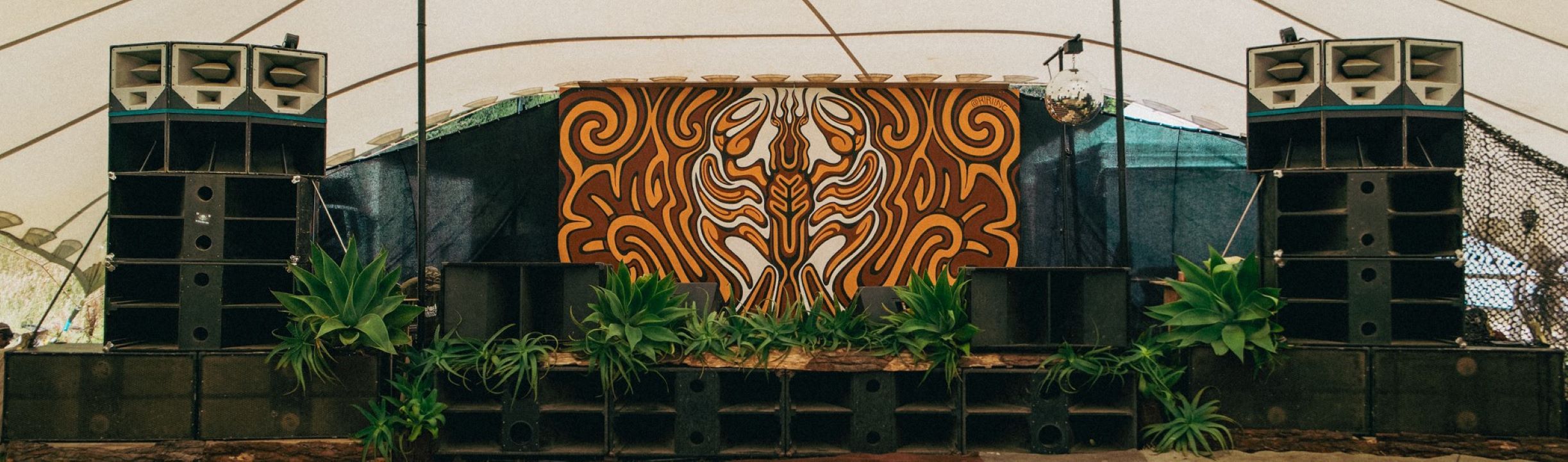 A stage absolutely surrounded by hefty speakers. The backdrop to the stage is an amazing painted kōura/freshwater crayfish.